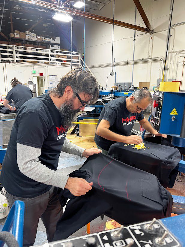 two men operating a screen printing machine currently printing a design on black hoodies