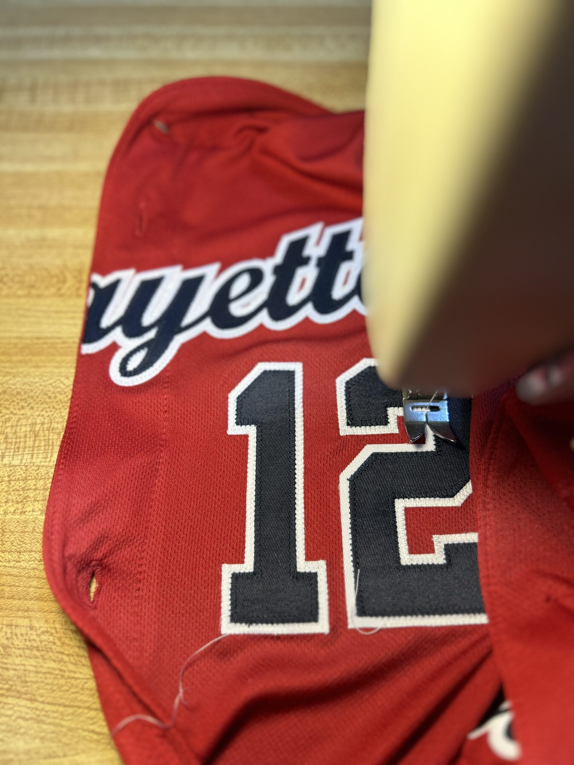 red jersey with black and white number 12 being sewn by a sewing machine in the foreground