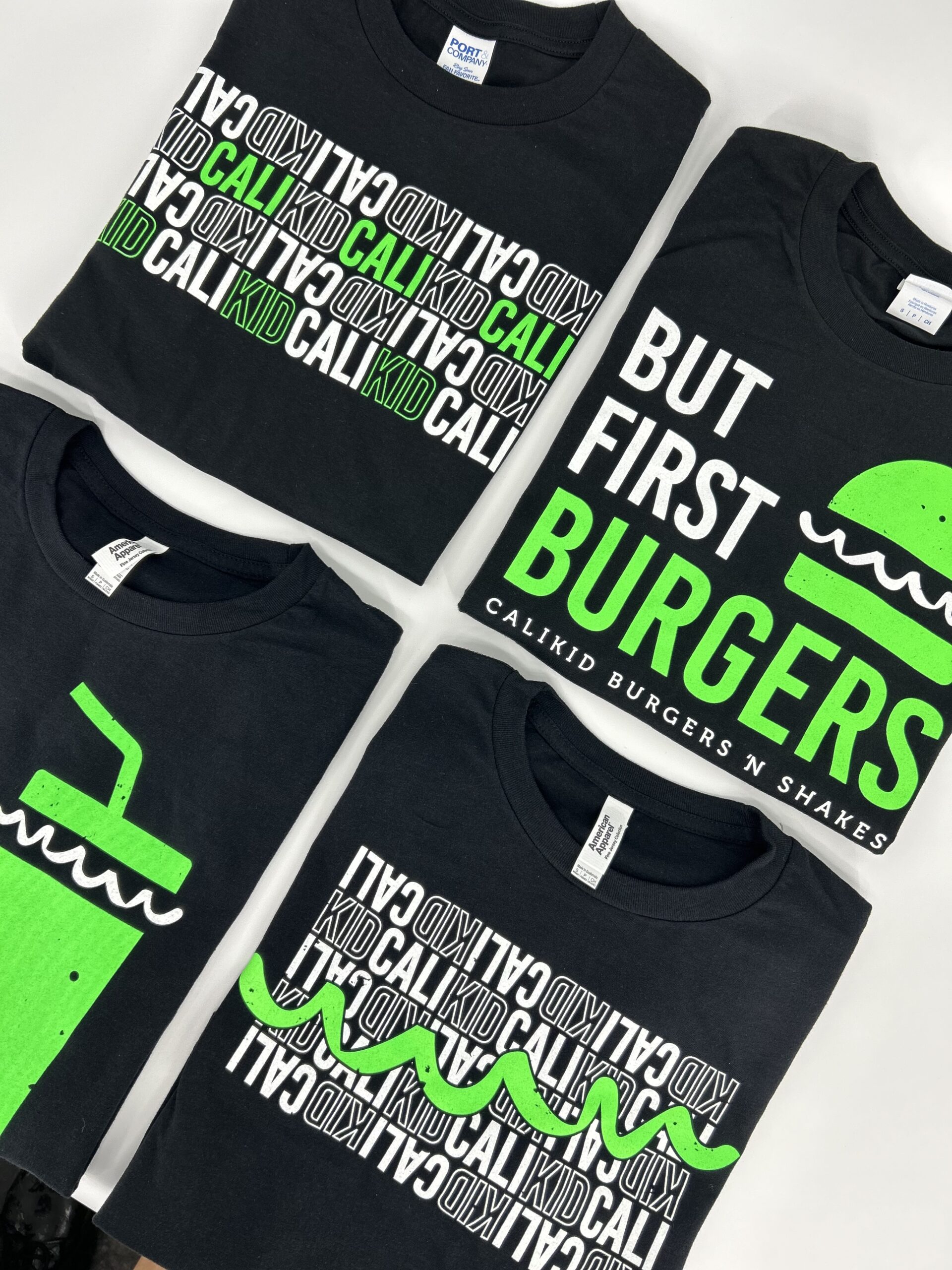 a close up of four black shirts for Cali Kid burgers N' Shakes with green and white designs