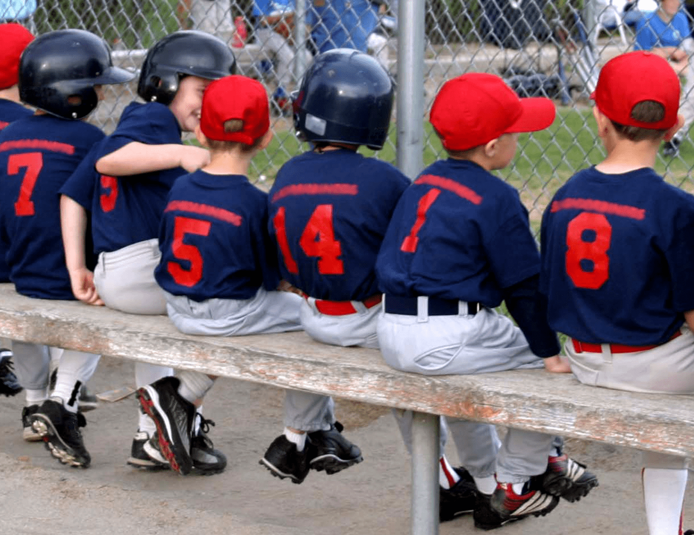 a young little league kids team in blue and red uniforms sitting on a wooden bench