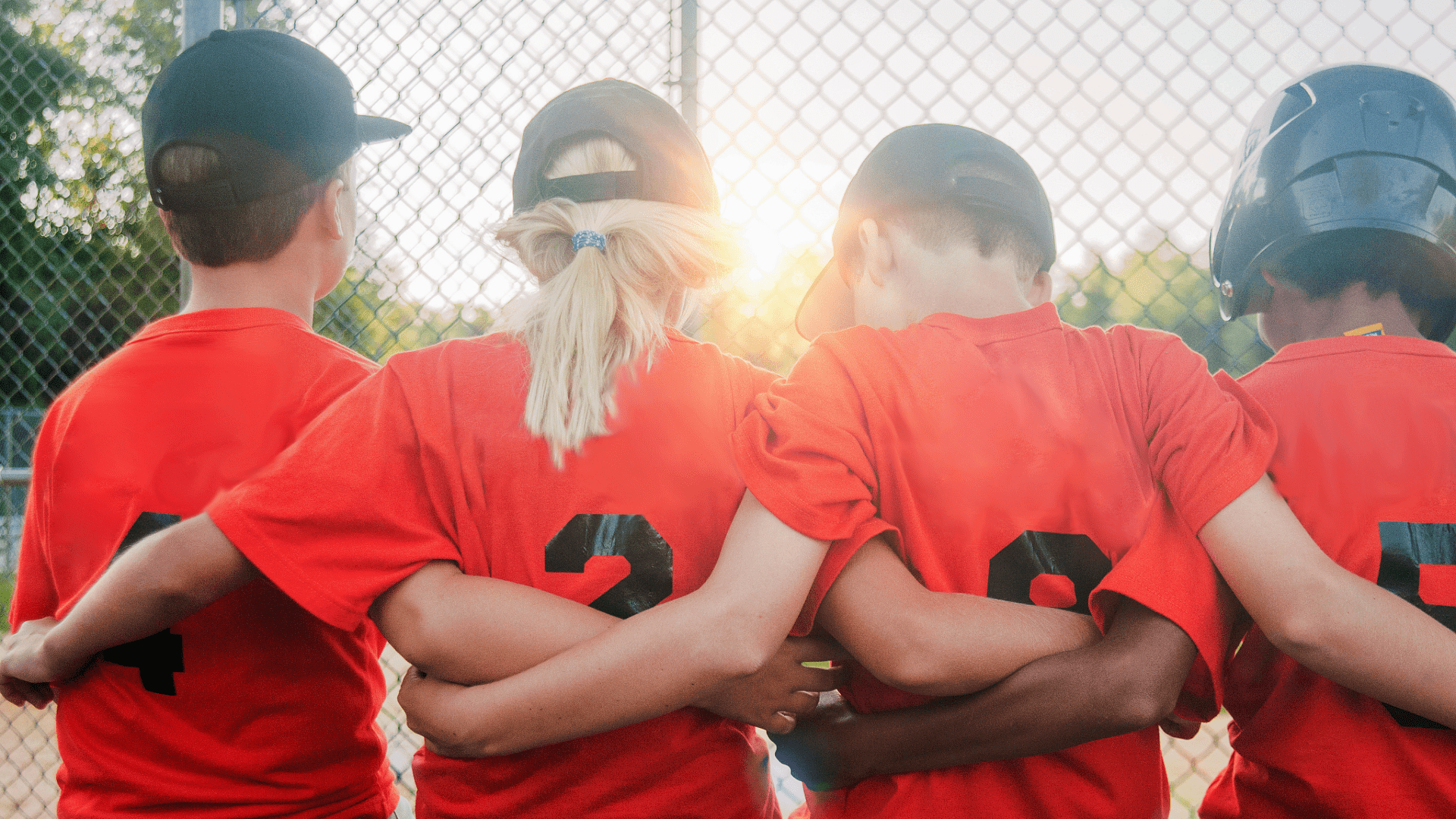 a team of little league players in orange jerseys with their arms around each other's backs