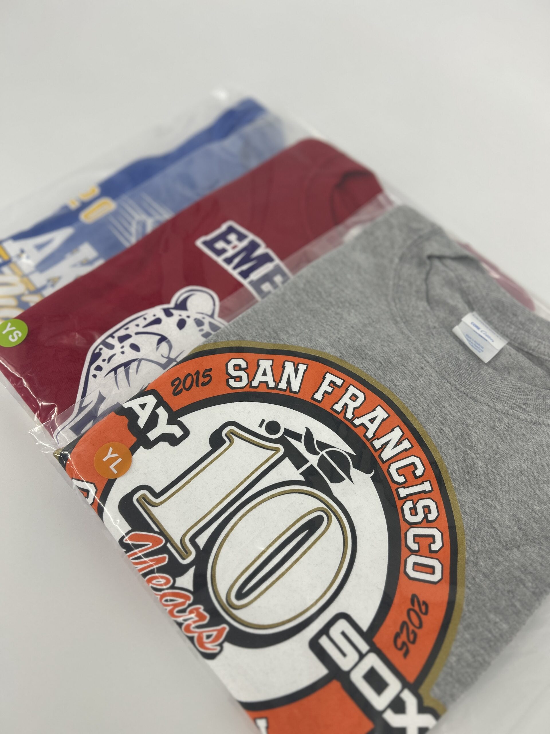 three different colored shirtsin plastic polybags, lined up in a row