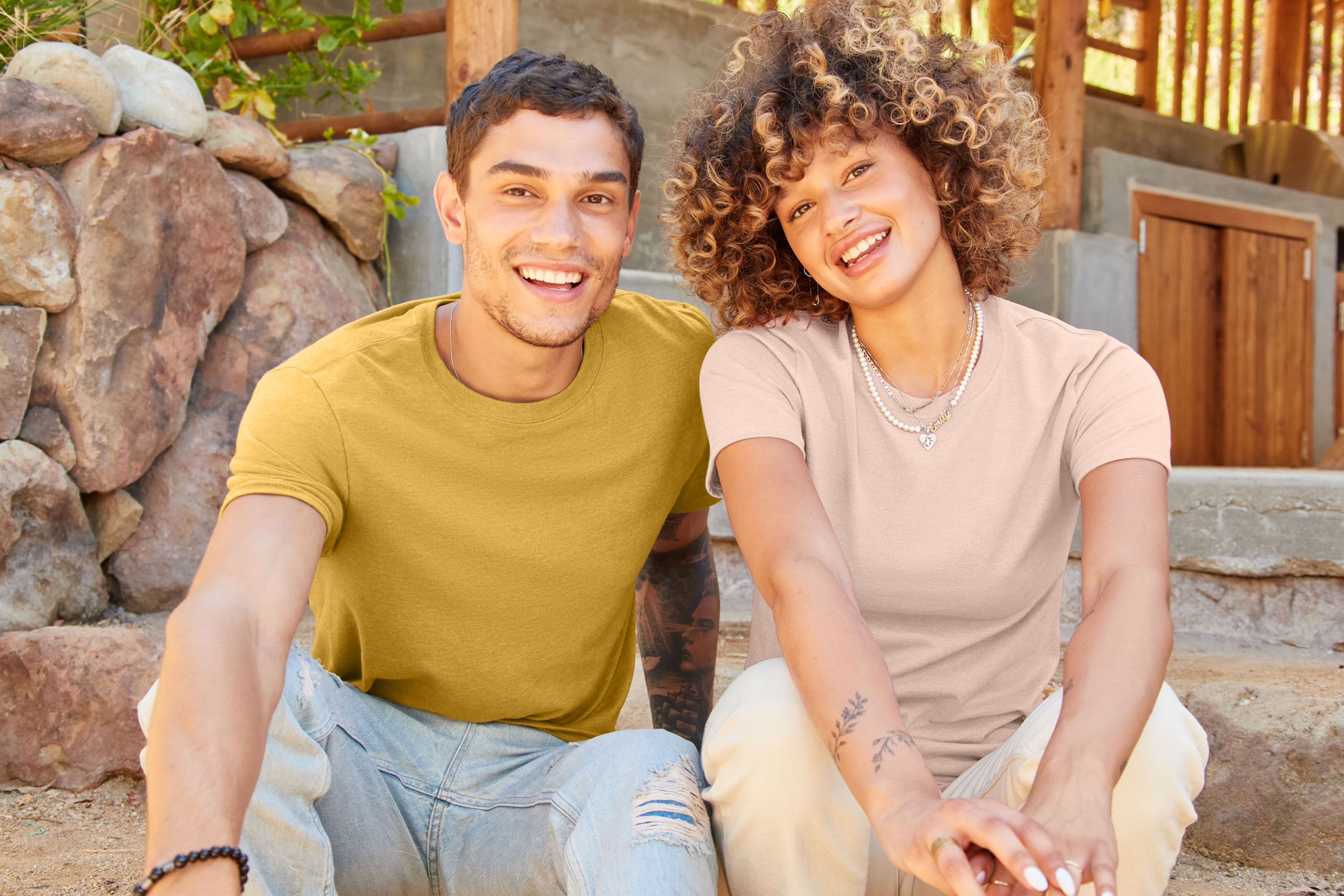a man and woman in mustard yellow and blush colored t-shirts sitting down and smiling at the camera