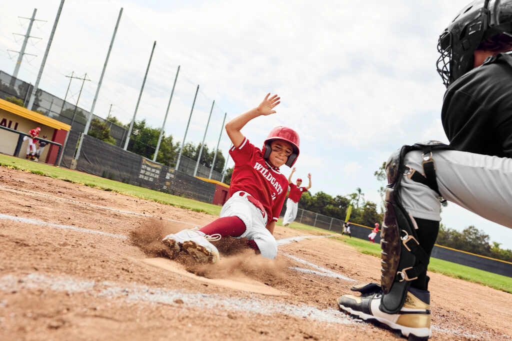 little league player in a red jersey sliding into home base with a catcher in the foreground